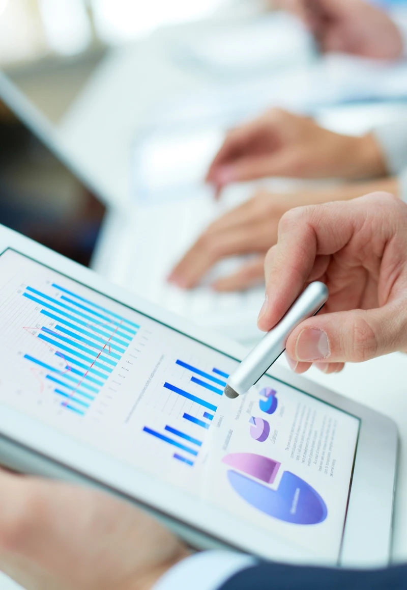 Profissional usando tablet com gráficos de desempenho e KPIs de facilities em reunião corporativa.