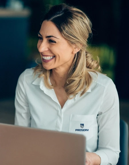 Colaboradora sorridente usando camisa branca com logotipo da empresa, atuando em escritório e transmitindo simpatia e confiança no atendimento.
