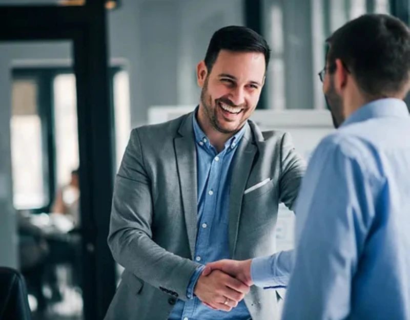 Empresário sorridente cumprimentando parceiro em ambiente corporativo, simbolizando relacionamento profissional