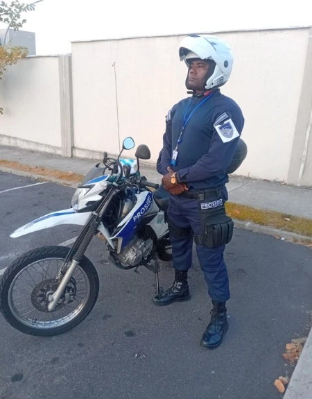 Agente de segurança em patrulhamento com moto, uniformizado e em atuação preventiva em área patrimonial.